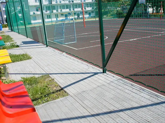 Kolorowe siedziska dla zawodników ustawione przy ogrodzonym boisku z nową nawierzchnią