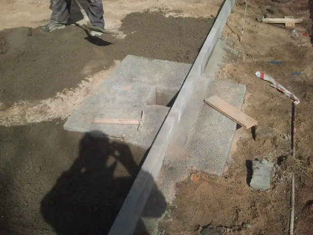 Robotnik zasypuje piaskiem betonową ławę fundamentową obok studzienki odwadniającej