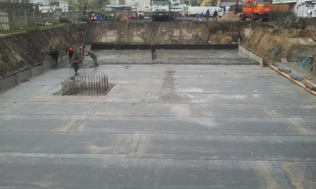 Pompa do betonu i dźwig pracują przy betonowaniu dużej płyty fundamentowej osiedla