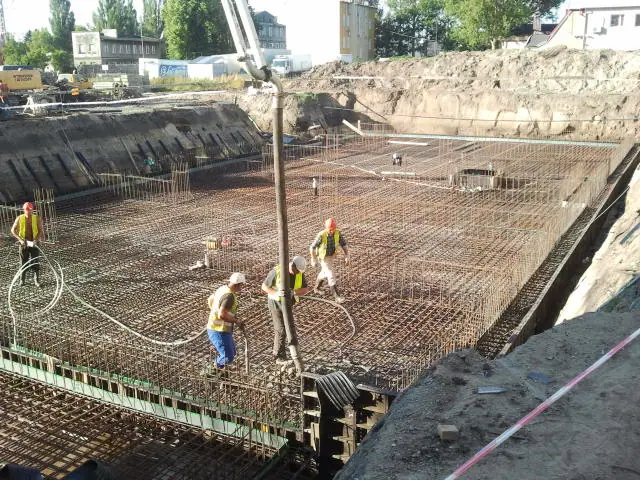 Robotnicy w kaskach betonują kolejną zbrojoną płytę na dnie głębokiego wykopu
