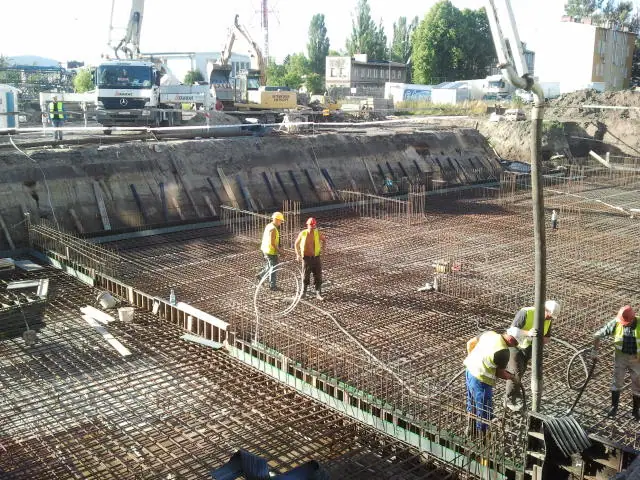 Ekipa z pompą do betonu i żurawiem betonuje rozległą zbrojoną płytę fundamentową