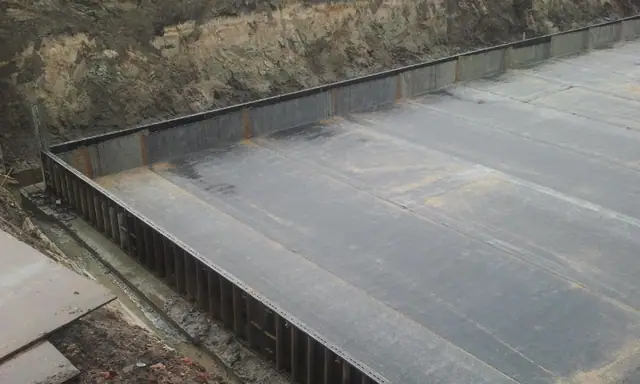 Czarna hydroizolacja pokrywa gotową płytę fundamentową osłoniętą stalowym szalunkiem wykopu