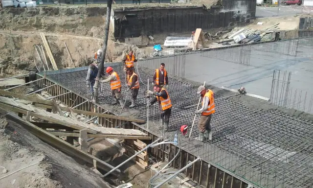 Ekipa w kamizelkach odblaskowych rozprowadza beton wężem pompy po zbrojonej płycie