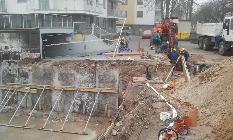 Geodeta mierzy wykop pod przyłącze kanalizacyjne niwelatorem obok ułożonych rur