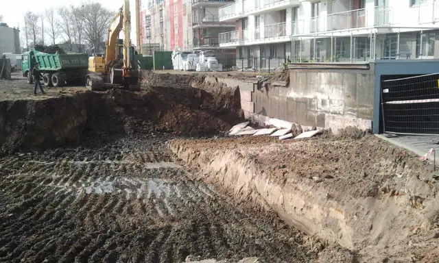 Koparka i wywrotka pracują w głębokim wykopie ziemnym na budowie Osiedla Bursztynowego