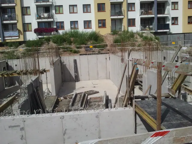 Wykop ze ścianami fundamentowymi tuż przy kolorowej elewacji sąsiedniego bloku mieszkalnego