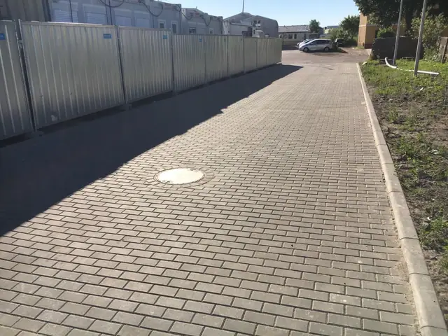 Droga z kostki brukowej ze studzienką kanalizacyjną prowadząca do parkingu przy blokach