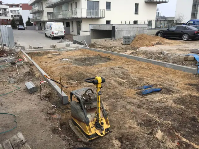 Wyrównany plac z geowłókniną i krawężnikiem przy budynkach, zaparkowane samochody osobowe
