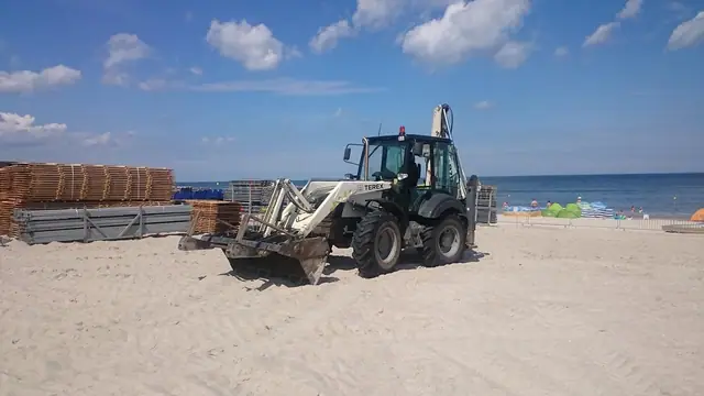 Koparko-ładowarka Terex pracuje przy elementach konstrukcyjnych na plaży podczas budowy areny Cavaliady