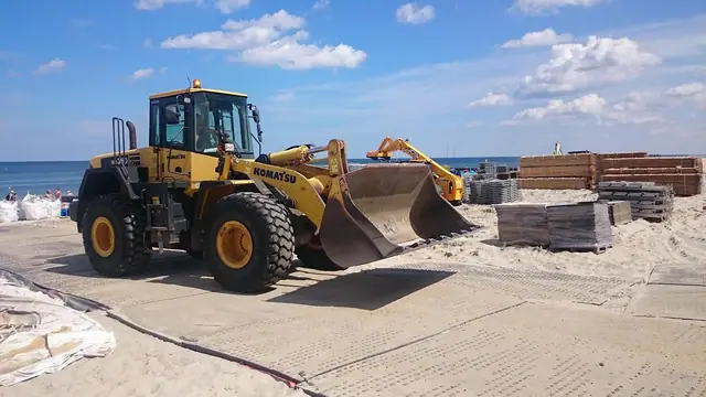 Ładowarka Komatsu manewruje przy paletach na plaży podczas budowy areny Cavaliady w Kołobrzegu
