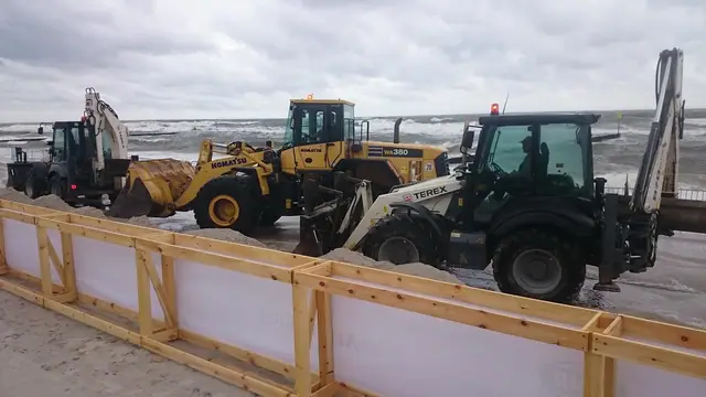 Trzy maszyny budowlane ustawione za drewnianym ogrodzeniem na plaży podczas budowy areny Cavaliady