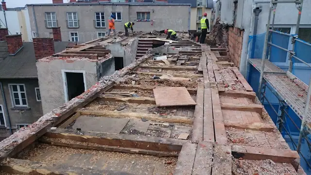 Ekipa demontuje więźbę dachową wzdłuż całej elewacji rozbieranego budynku