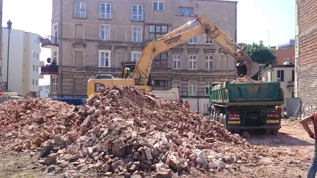 Hałda ceglanego gruzu po rozbiórce z pracującą w tle koparką