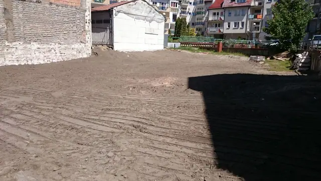 Częściowo wyrównany teren po rozbiórce z pryzmą ziemi i czarną nawierzchnią