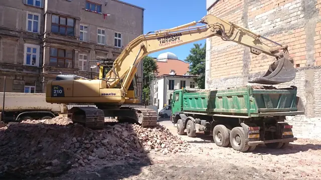Koparka ładuje łyżką gruz z rozbiórki na skrzynię samochodu ciężarowego
