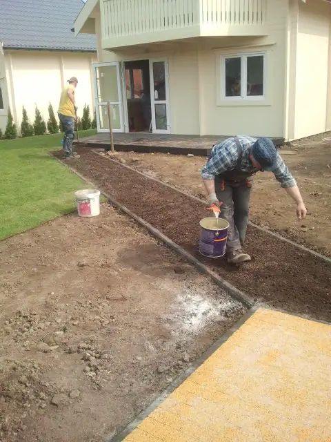 Pracownik maluje żółtą linię przy krawędzi ścieżki tuż przed wejściem do budynku