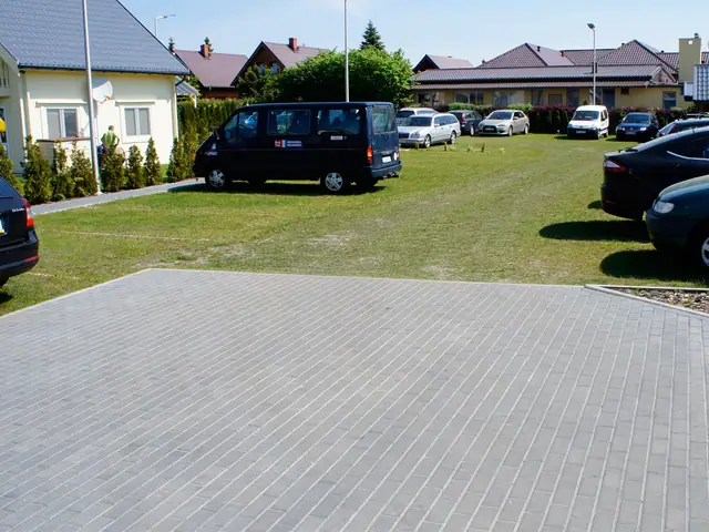 Szeroki wybrukowany plac parkingowy z busem i samochodami przy domkach letniskowych