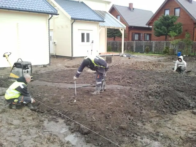 Ekipa wytycza sznurkiem układ nawierzchni w błotnistym terenie przy ścianie budynku