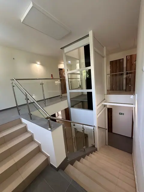 Klatka schodowa ze szklaną balustradą i przeszkloną windą widziana z górnego podestu