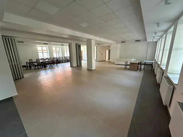 Duża wielofunkcyjna sala z długim pasem okien, stołami i sofą gotowa do wyposażenia