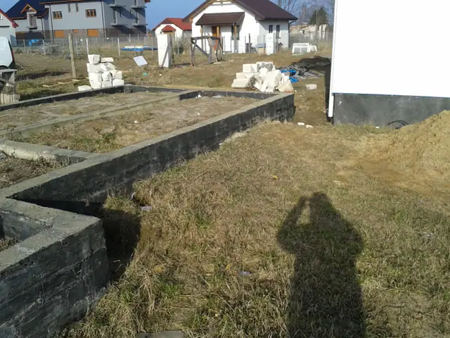 Fundament z pustaków przy zabudowie jednorodzinnej, cień fotografującego widoczny na trawniku