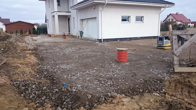 Utwardzony tłuczniem plac przed domem z pomarańczową rurą kanalizacyjną na powierzchni