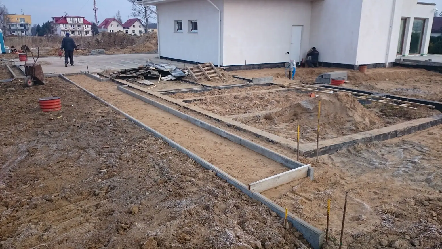 Betonowa opaska fundamentowa wokół domu z widocznymi przyłączami kanalizacyjnymi – wyjście kanalizacji, które ma znaczenie przy podłączeniu szamba