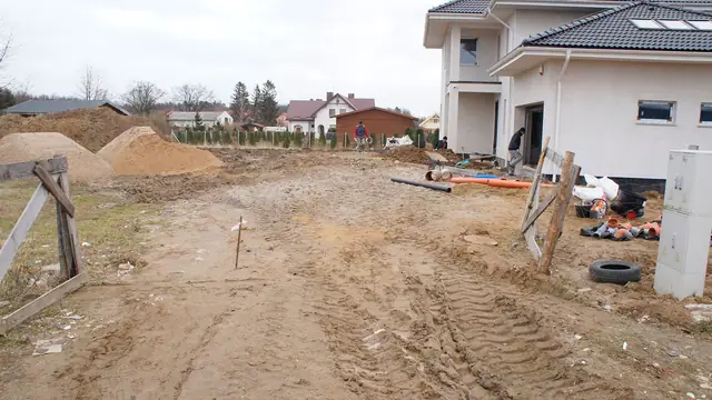 Plac budowy przed domem jednorodzinnym z kopcami piasku i śladami kół na gruncie