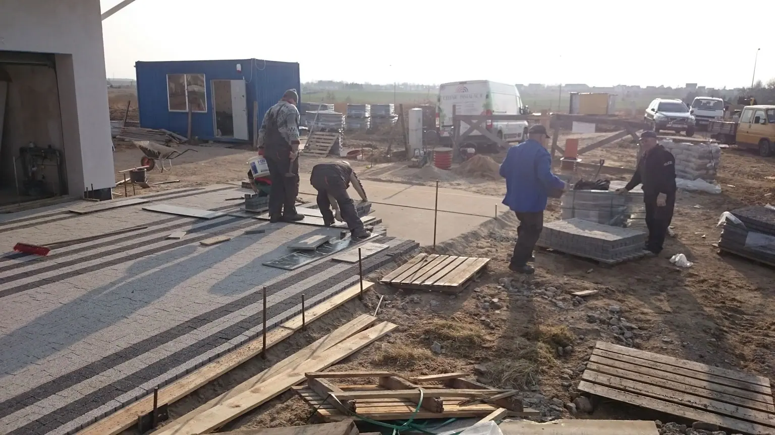 Robotnicy układają kostkę brukową w geometryczny wzór na podjeździe przed domem jednorodzinnym