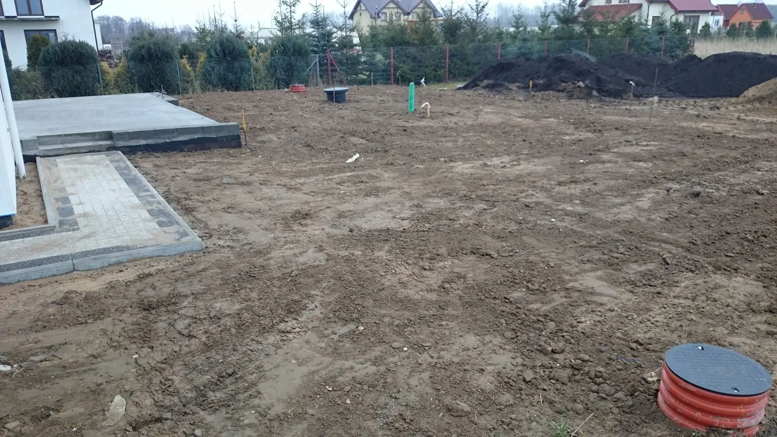 Wytyczony teren pod nawierzchnię przy domu jednorodzinnym, obok kręgi kanalizacyjne – planowanie instalacji przed ułożeniem kostki