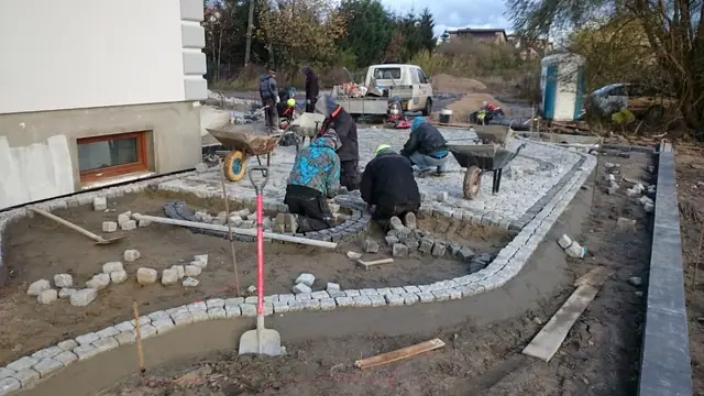 Ekipa układa granitowy obrzeżnik wzdłuż ścieżki, w tle betoniarka i taczka