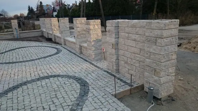 Rząd murowanych kamiennych słupków wzdłuż gotowego podjazdu z kostki brukowej