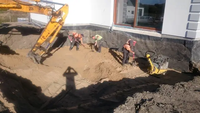 Koparka i ekipa wykonują wykop wzdłuż fundamentu domu pod dalsze prace ziemne