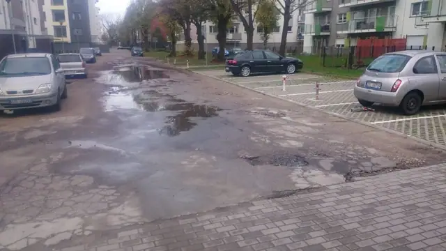 Zniszczona droga wewnętrzna z kałużami i ubytkami przy parkingu na ulicy Wielkopolskiej w Kołobrzegu
