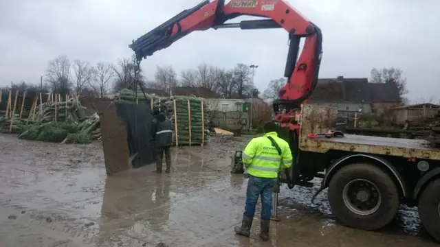 Żuraw hydrauliczny ciężarówki rozładowuje betonową płytę drogową na błotnistym placu