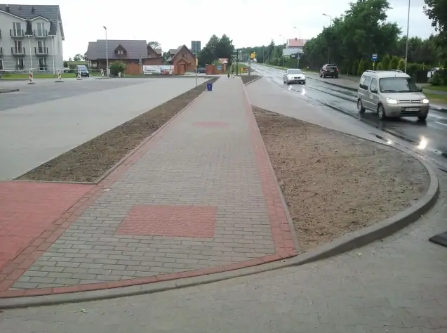 Wykończona zakrzywiona ścieżka z czerwonym akcentem dekoracyjnym z kostki przy mokrej jezdni