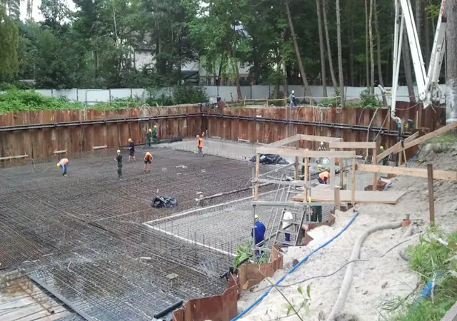 Pompa do betonu i ekipa wylewają fundament w głębokim wykopie budowy hotelu