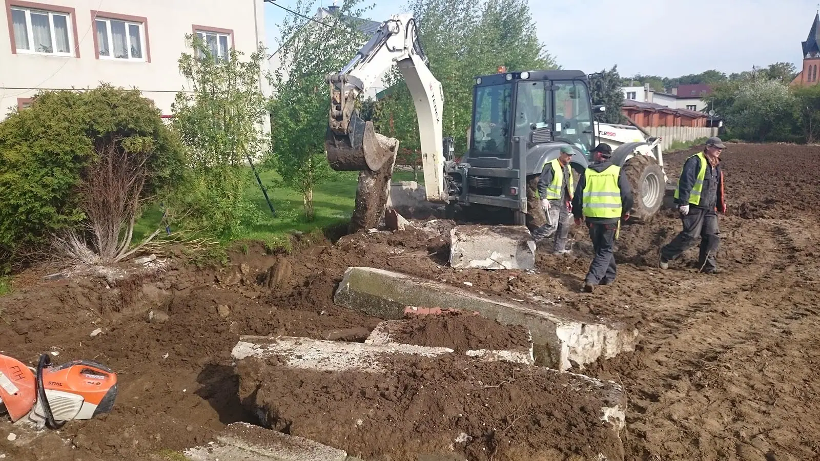 Koparka i robotnicy demontują stary betonowy płot na granicy działki w Ustroniu Morskim przed budową nowego ogrodzenia