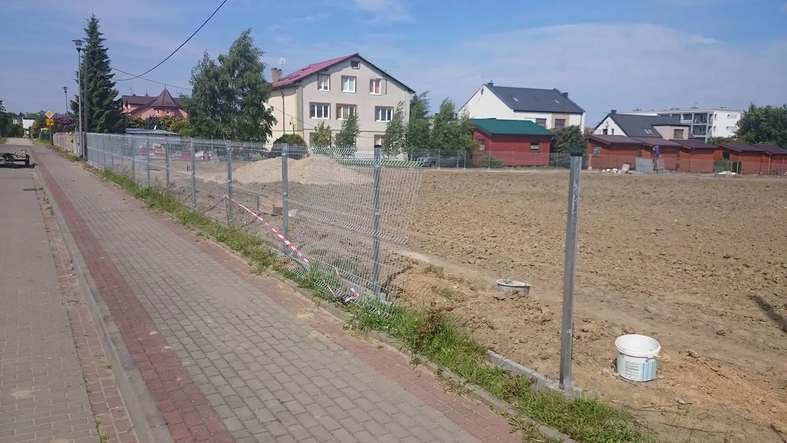 Gotowe ogrodzenie z siatki na stalowych słupkach wzdłuż nowego chodnika z kostki brukowej