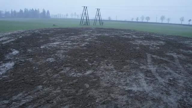 Błotnisty plac manewrowy przy elektrowni wiatrowej ze śladami pracy maszyn budowlanych