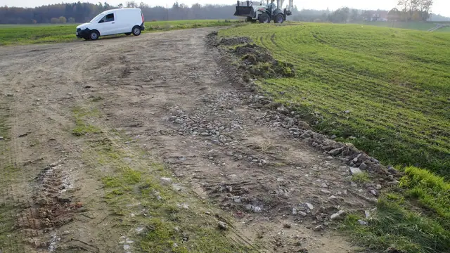 Droga dojazdowa wśród zielonych pól z koparką i samochodem dostawczym w tle