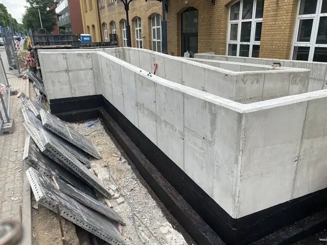 Ukończona betonowa ściana oporowa z czarną hydroizolacją i złożonymi panelami szalunkowymi