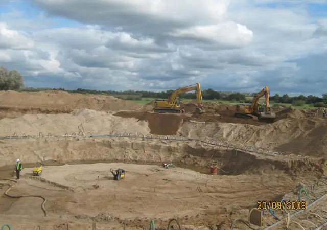 Dwie koparki pracują w szerokim, okrągłym wykopie pod fundament turbiny wiatrowej
