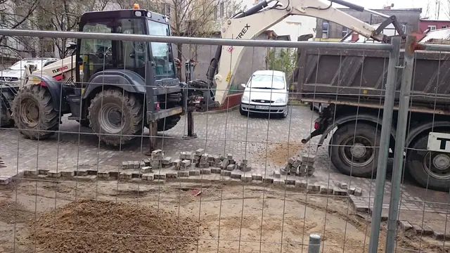 Koparko-ładowarka i ciężarówka na drodze przy rozłożonych elementach nowego krawężnika