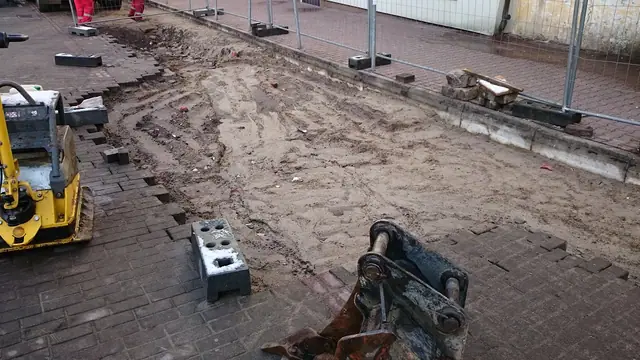 Minikoparka pracuje na częściowo rozebranym chodniku z czerwonej kostki brukowej