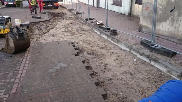 Błotnisty pas rozebranej nawierzchni z czerwonej kostki z podporami geodezyjnymi w tle