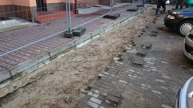 Fragment rozebranego chodnika z czerwonej kostki obok zaparkowanego samochodu osobowego