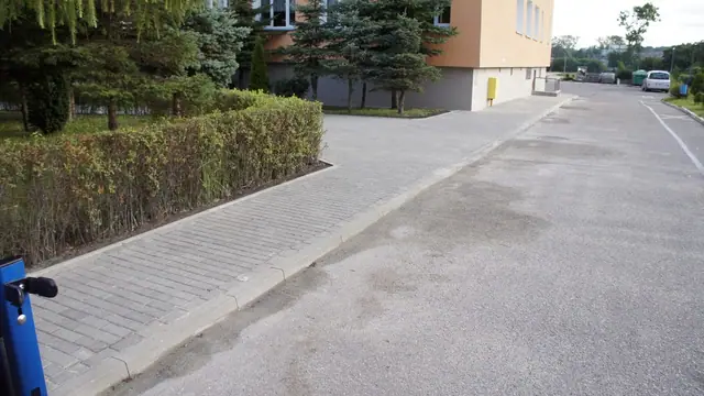 Chodnik z kostki wzdłuż żywopłotu prowadzący w stronę parkingu przy szkole