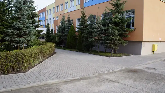 Chodnik z kostki brukowej między żywopłotami prowadzący do budynku szkoły