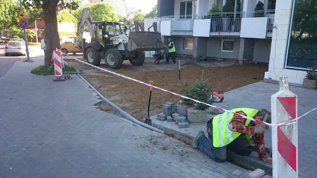 Koparko-ładowarka i pracownik przygotowują podbudowę pod kostkę brukową przed wejściem do hotelu